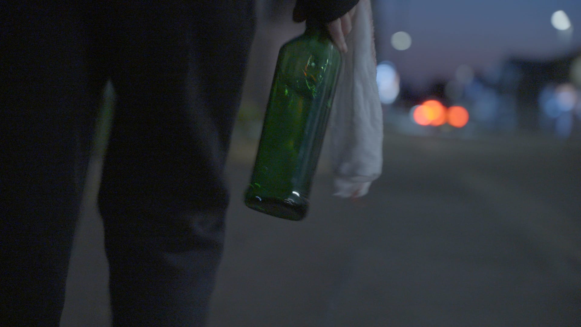A still from Stop The Boats showing a hand holding a green bottle at night